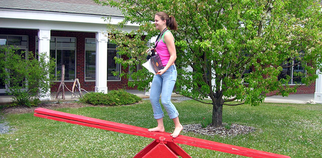 a highschool aged girl standing midway on a seesaw