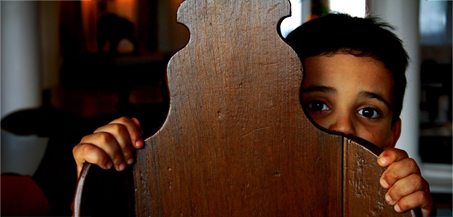 a boy hiding behind a chair looking fearful