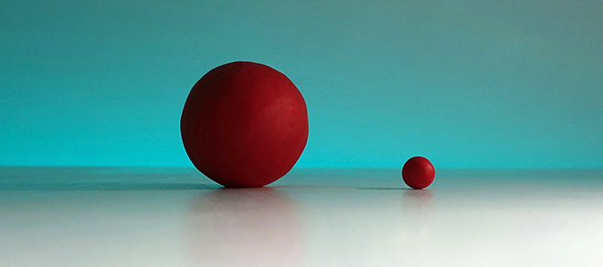 Clay - an image of 2 red clay balls on a flat reflective surface, one ball much larger than the other